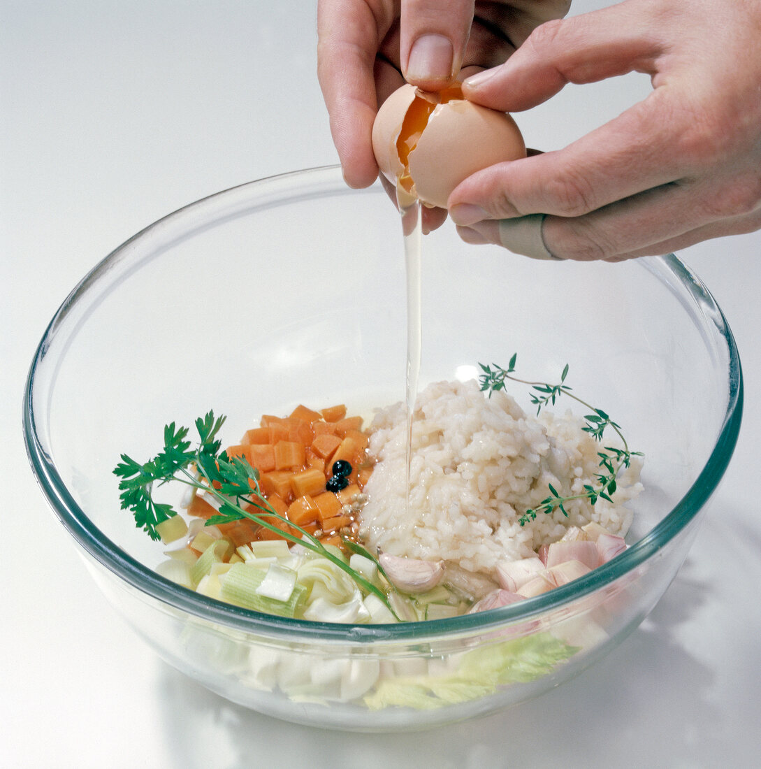 Close-up of hand adding egg yolk in bowl with fresh vegetables and herbs, step 2