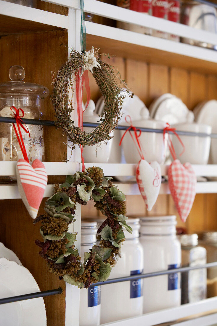 Wreath of twigs and cones with fabric hearts hanging on kitchen shelf