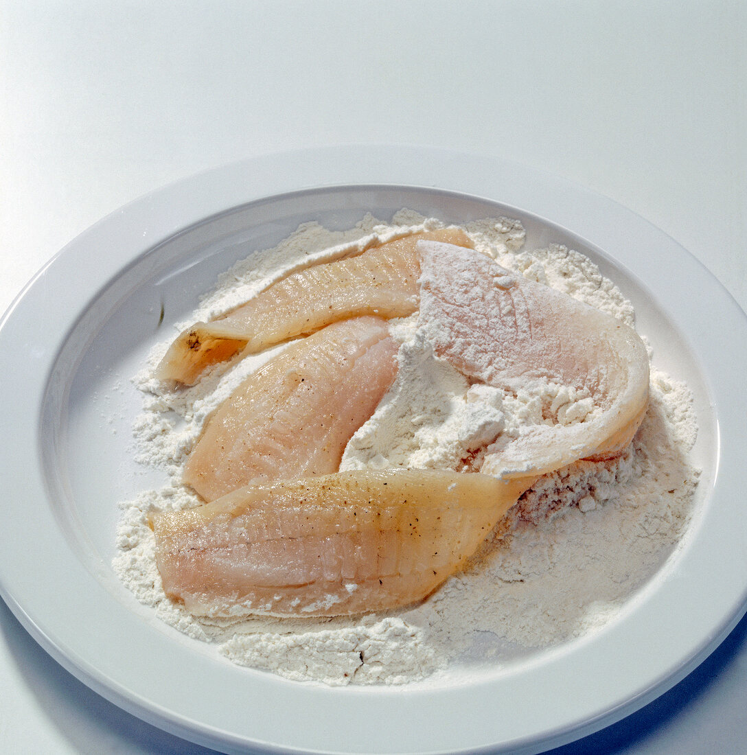Close-up of plaice fillets in flour on plate, step 1