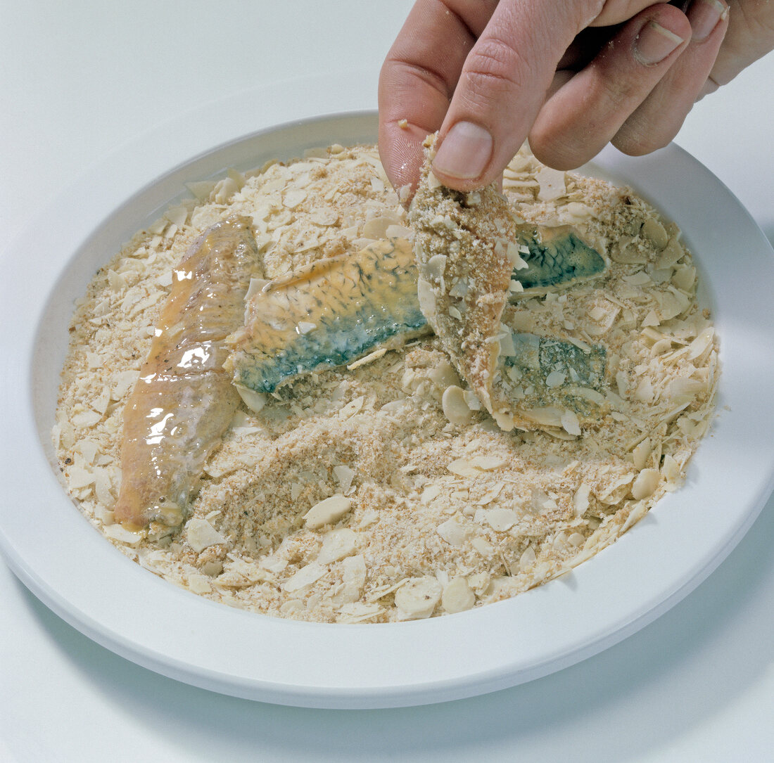 Close-up of hand covering roach fish fillets with almonds and breadcrumbs, step 3