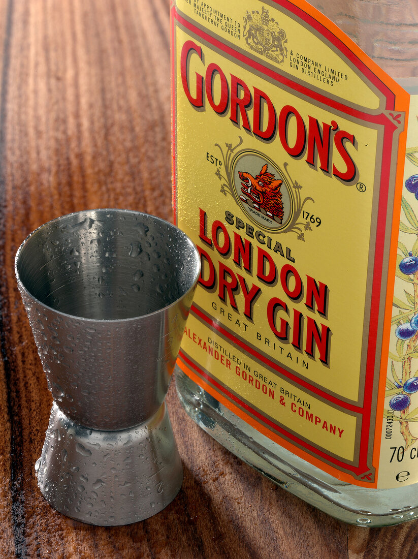 Close-up of gin bottle and measuring cup on wooden table