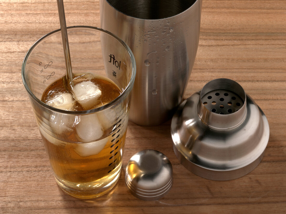 Close-up of whiskey with ice cubes besides shaker