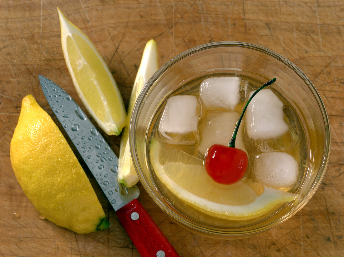Twist drink in glass with ice cubes, cherry and lemon