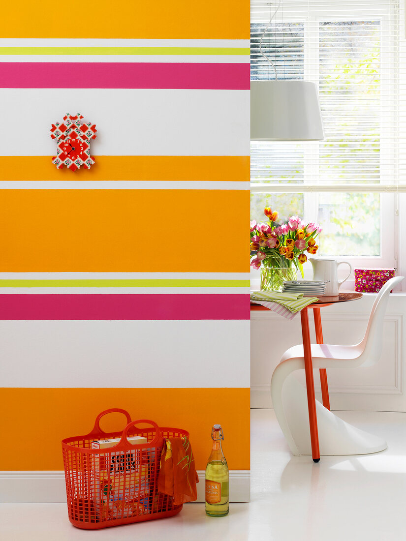 Red basket in front of colourful striped wall with view of dining room