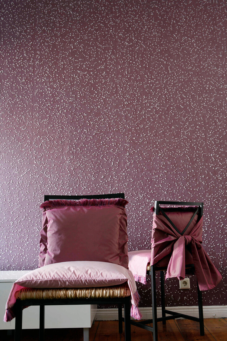 Chairs with pink fringed pillows against bubble patterned wallpaper