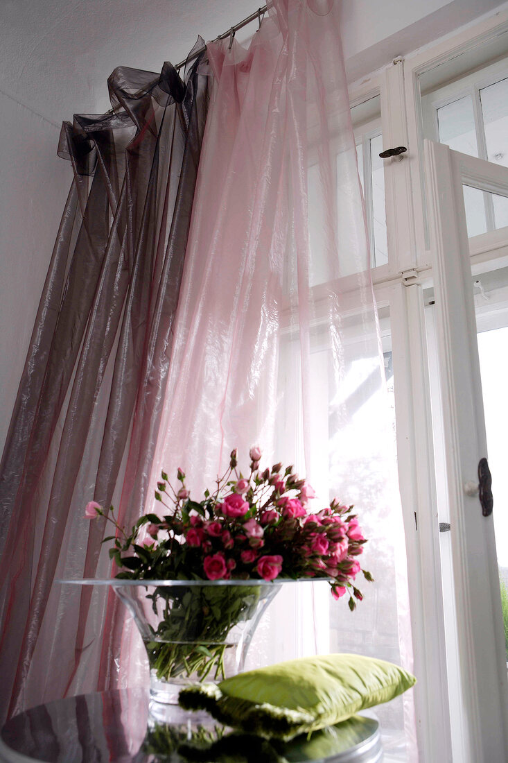 Fresh roses in glass vase against transparent curtains