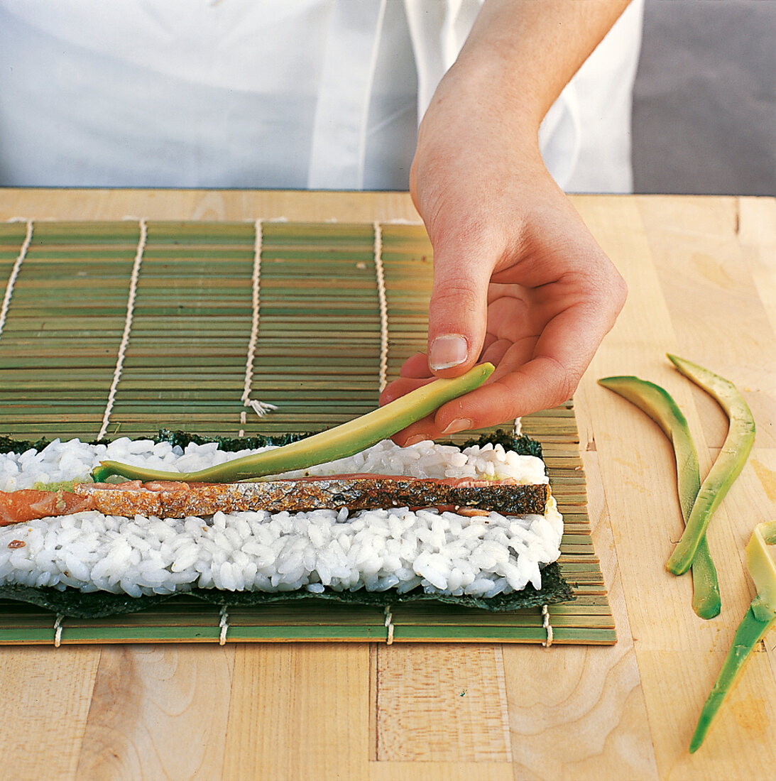 Sushi - Lachs- und Avocadostreif en werden auf Reis gelegt