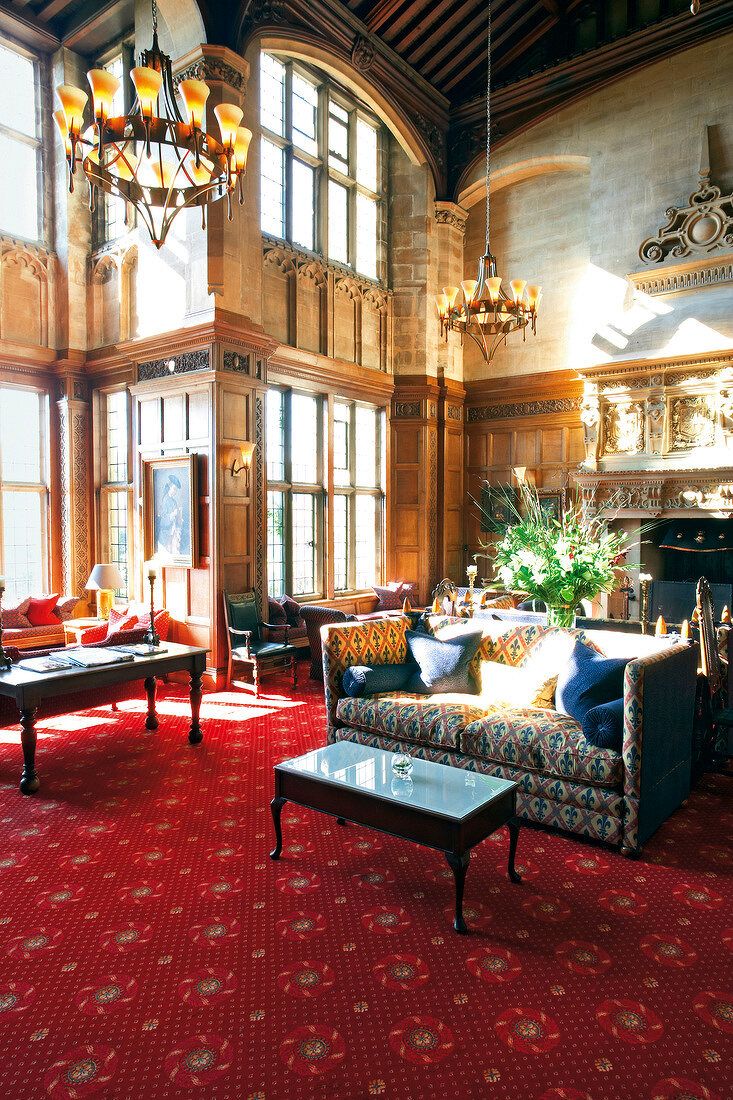 Fireplace room in hotel Bovey Castle with chandeliers, red carpet and sofas, Devon, UK