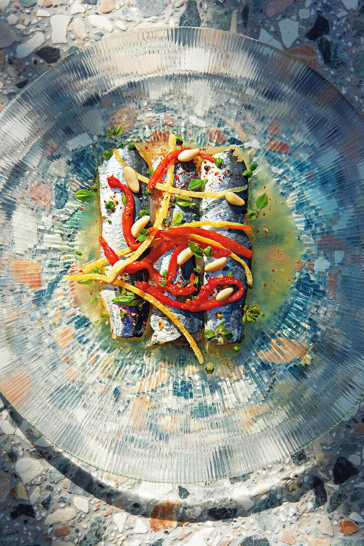 Sardines marinated with peppers, pine nuts and lemon juice on glass plate