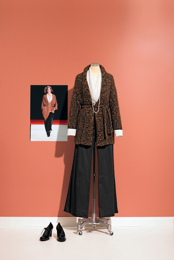 Knitted jacket and black pants styled by Paul Smith on clothes stand with photo of model