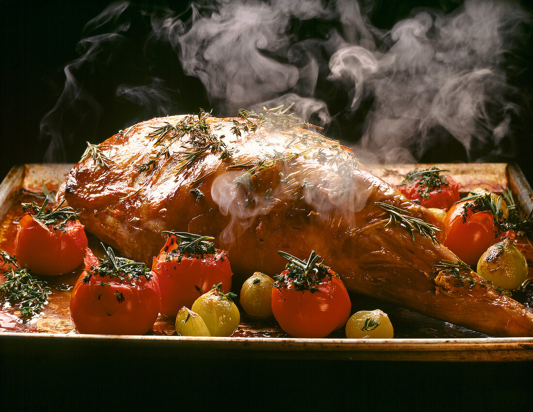 Roast leg of lamb with herb, shallots and tomatoes in baking dish