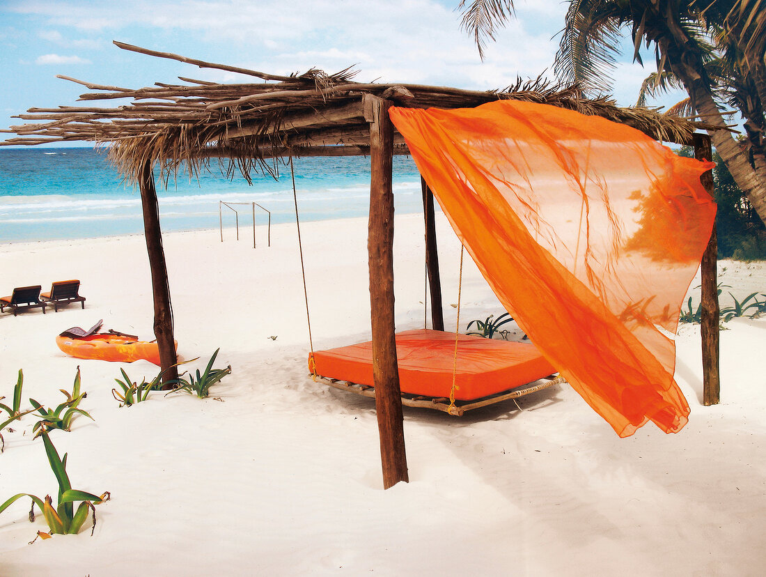 Four-poster bed made of wood with orange curtain and mattress on the beach, Mexico