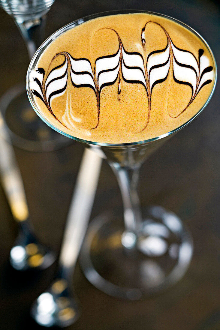 Espresso decorated with milk foam and chocolate sauce in shape of waves in cocktail glass