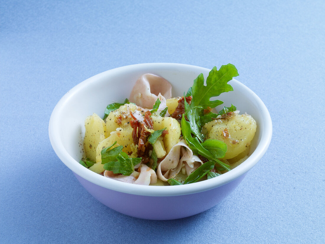 Potato salad with mortadella, arugula and basil in bowl