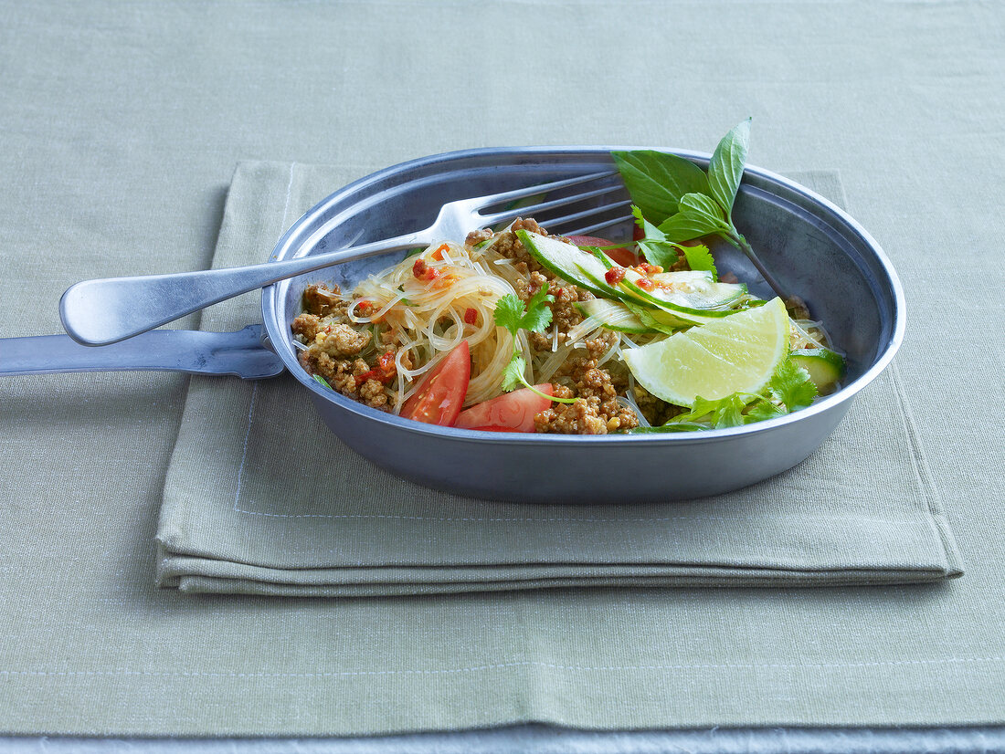 Thai noodle salad with beef, lime, tomatoes and coriander in pan and fork
