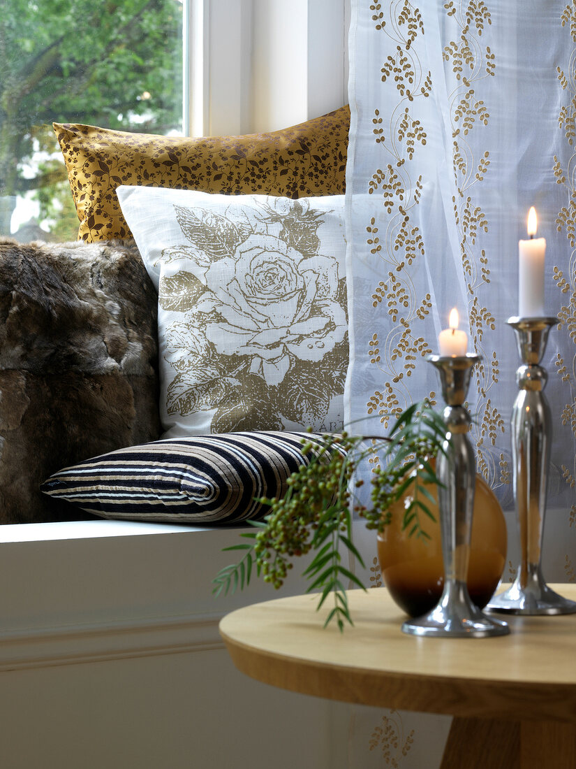 Lit candles and curtain in front of cushions on window sill