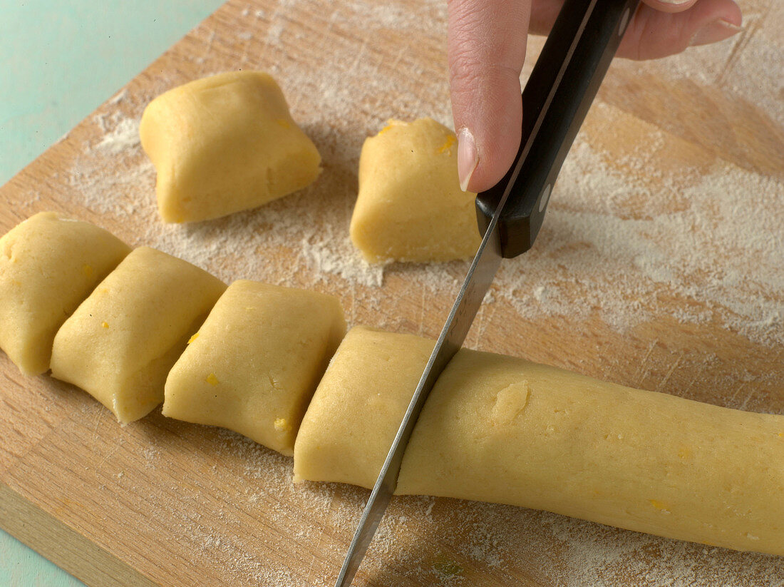 Close-up of rolled dough being cut in pieces for preparation of biscuits, step 2