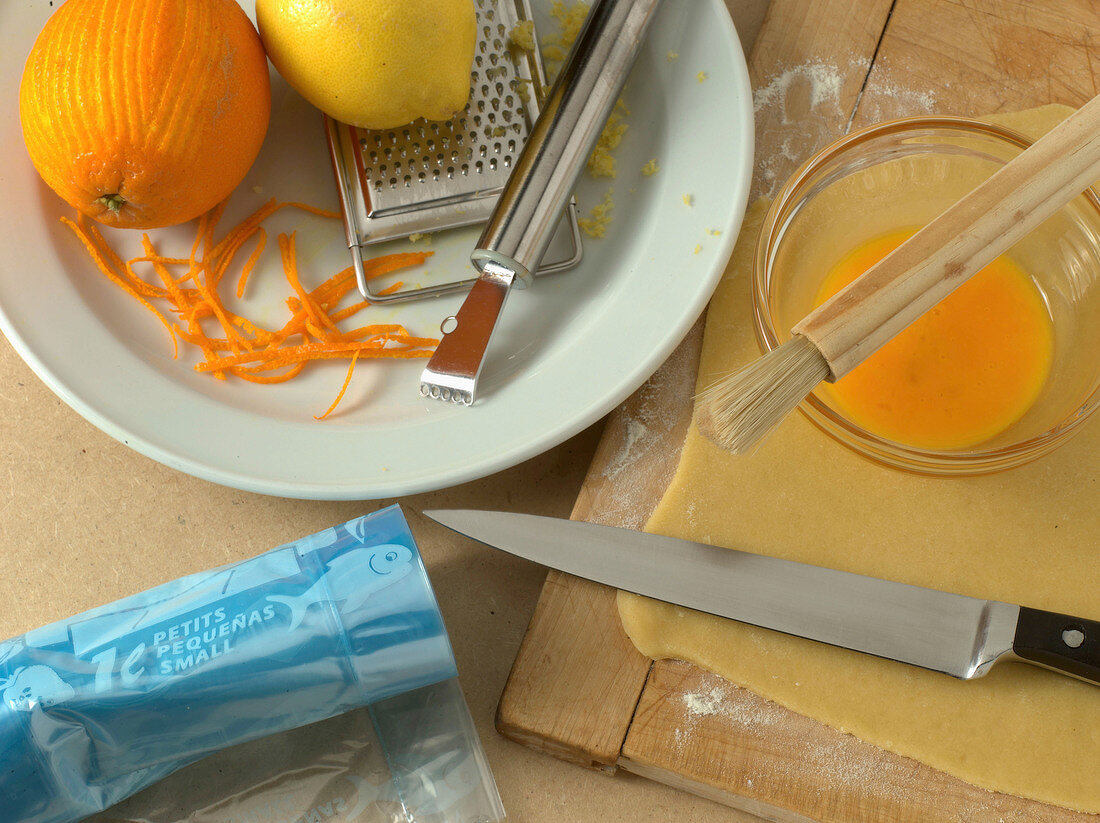 Orange and lemon with grater on plate, brush and knife on wooden board