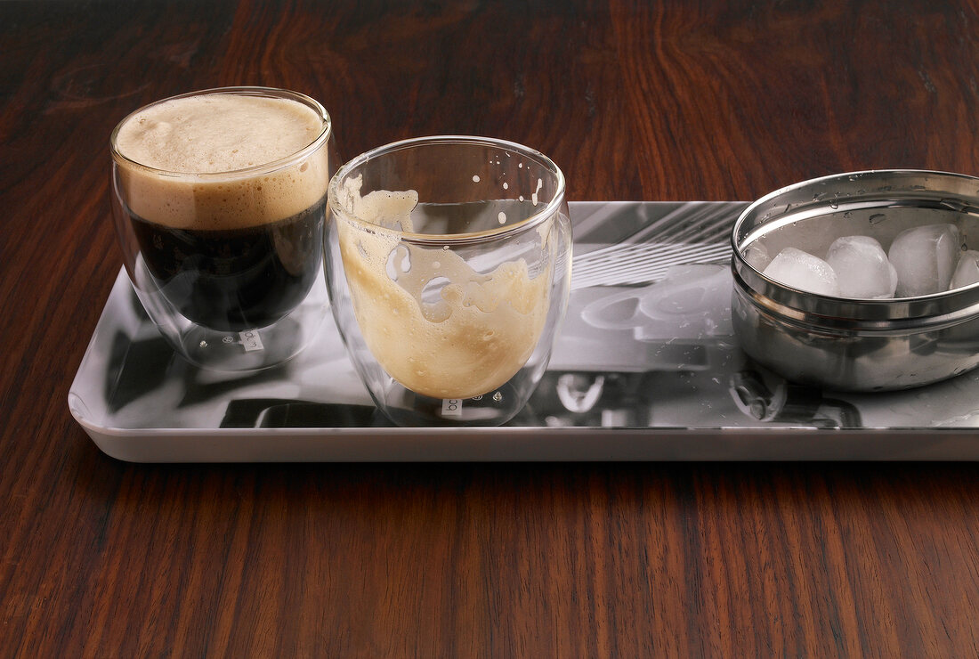 Glass of espresso shakerato con rosa and bowl of ice cubes in serving dish