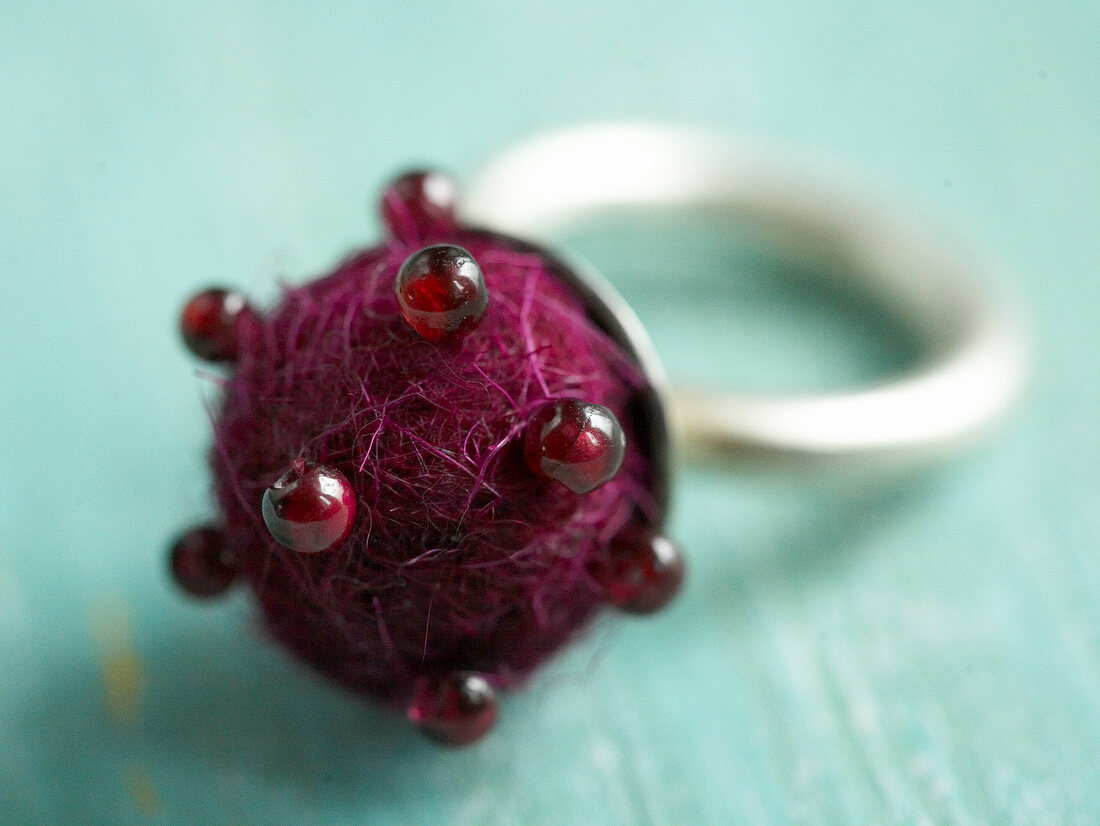 Close-up of embroidered silver finger ring with red felt ball