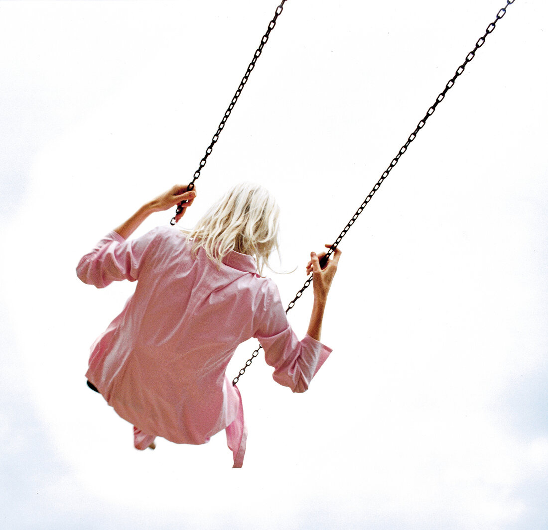 Rear view of blonde woman in pink blouse swinging on swing