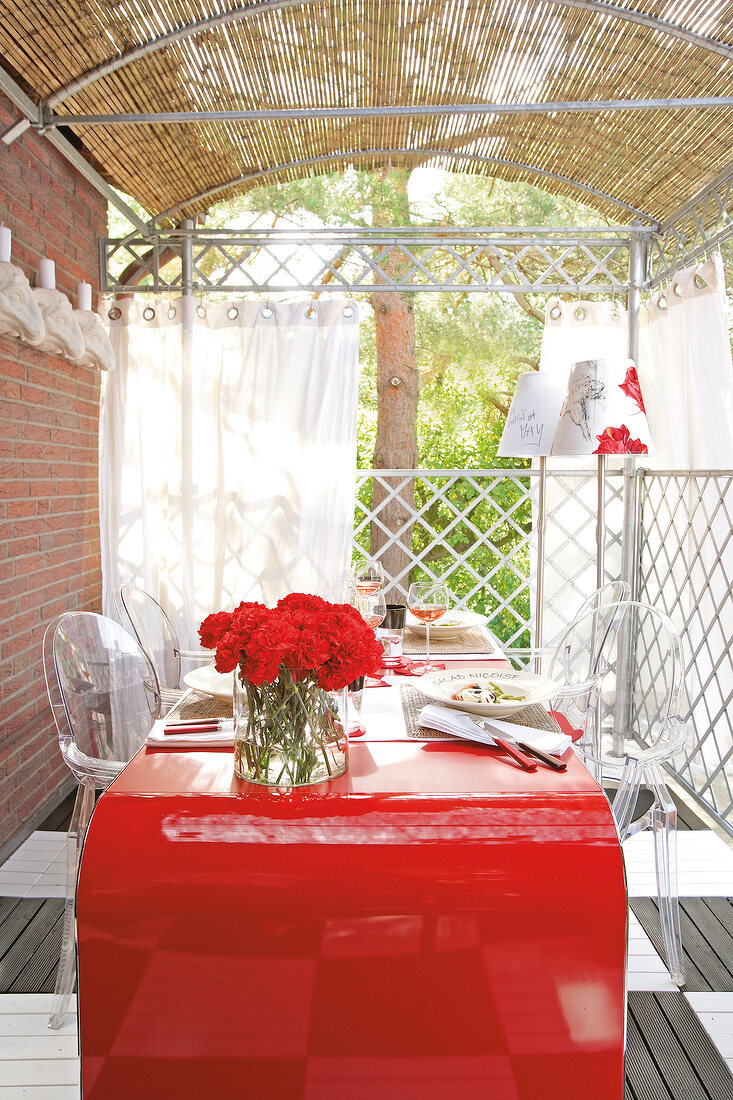 Balkon mit imposantem roten Tisch und transparenten Stühlen