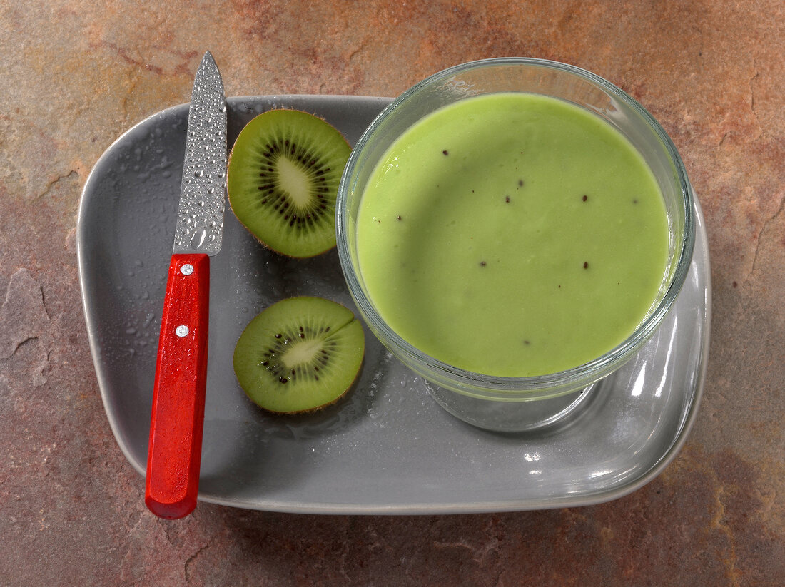 Green light juice in glass with kiwi slices and knife in serving dish