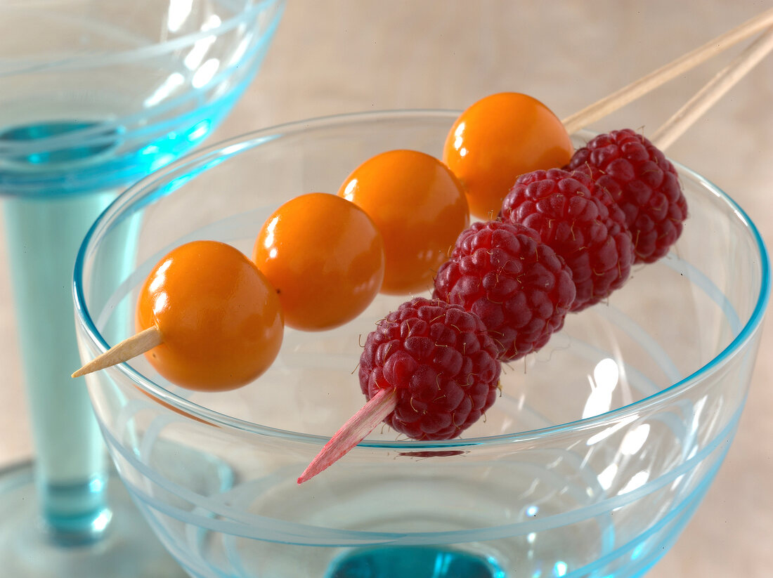 Two fruit skewers with raspberries and physalis on empty cocktail glass