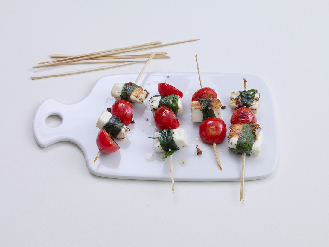Four wild garlic skewers with sheep cheese and cherry tomatoes on chopping board