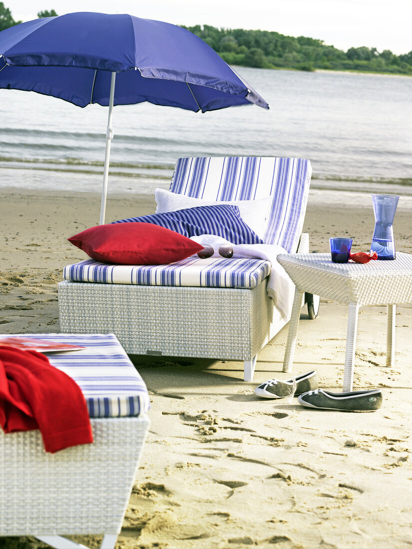 White sun loungers, table and beach umbrella with blue, white and red cushions on beach