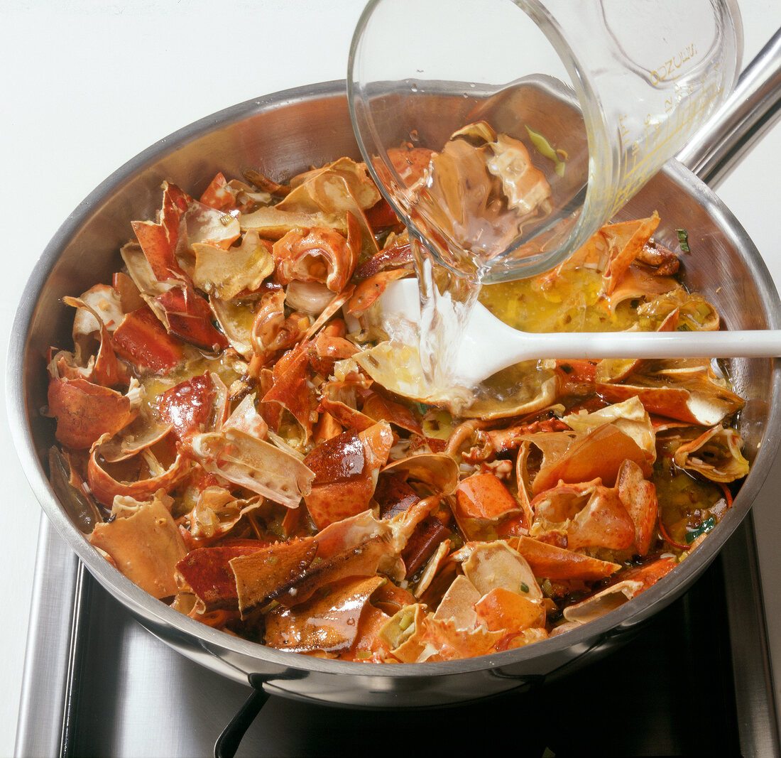 Water being poured to vegetables and lobster carcasses in wok, step 4