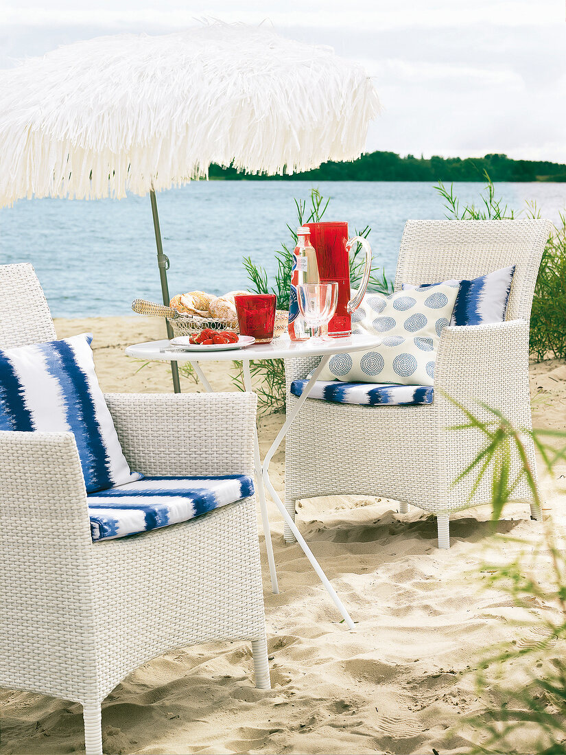gedeckter Tisch und 2 Sessel am Strand, weißer Sonnenschirm