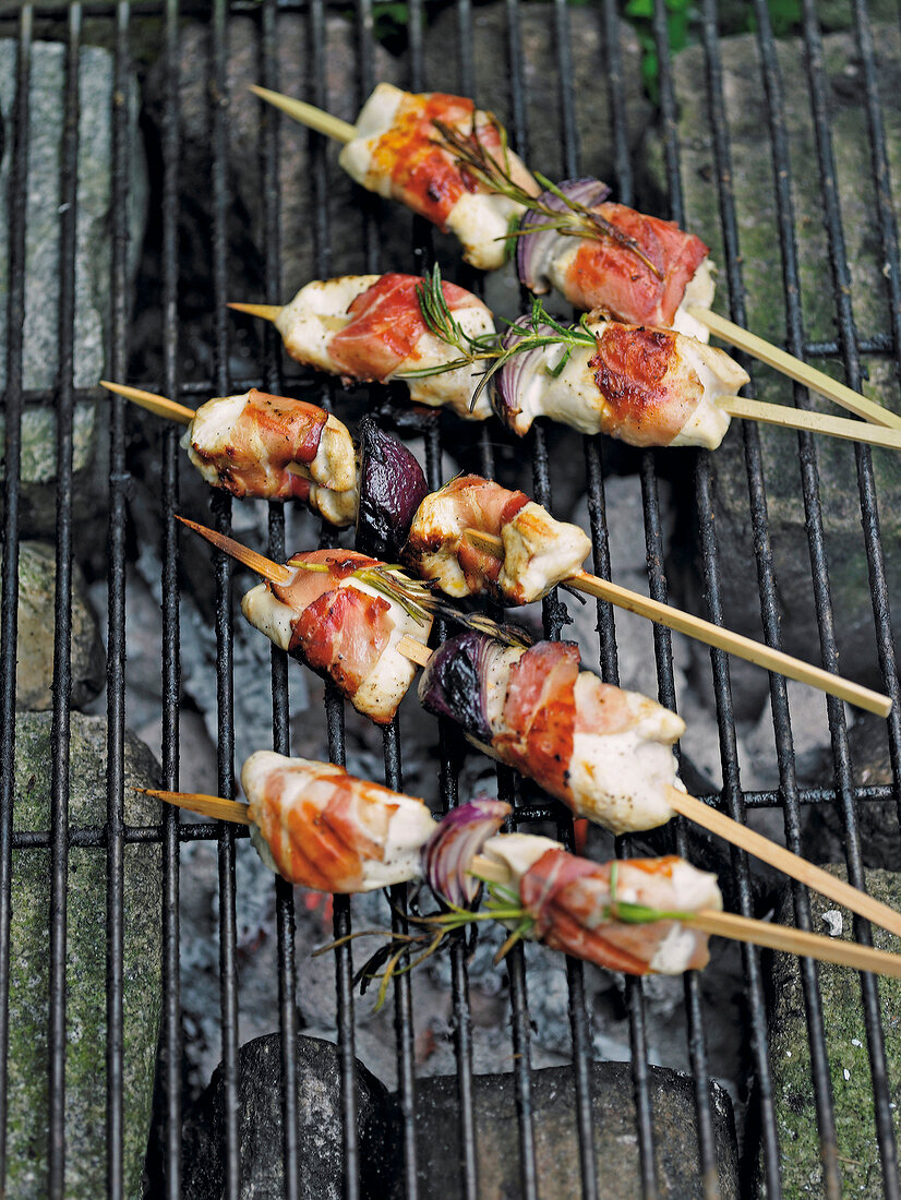 Chicken with ham, onions and rosemary in skewers on grill