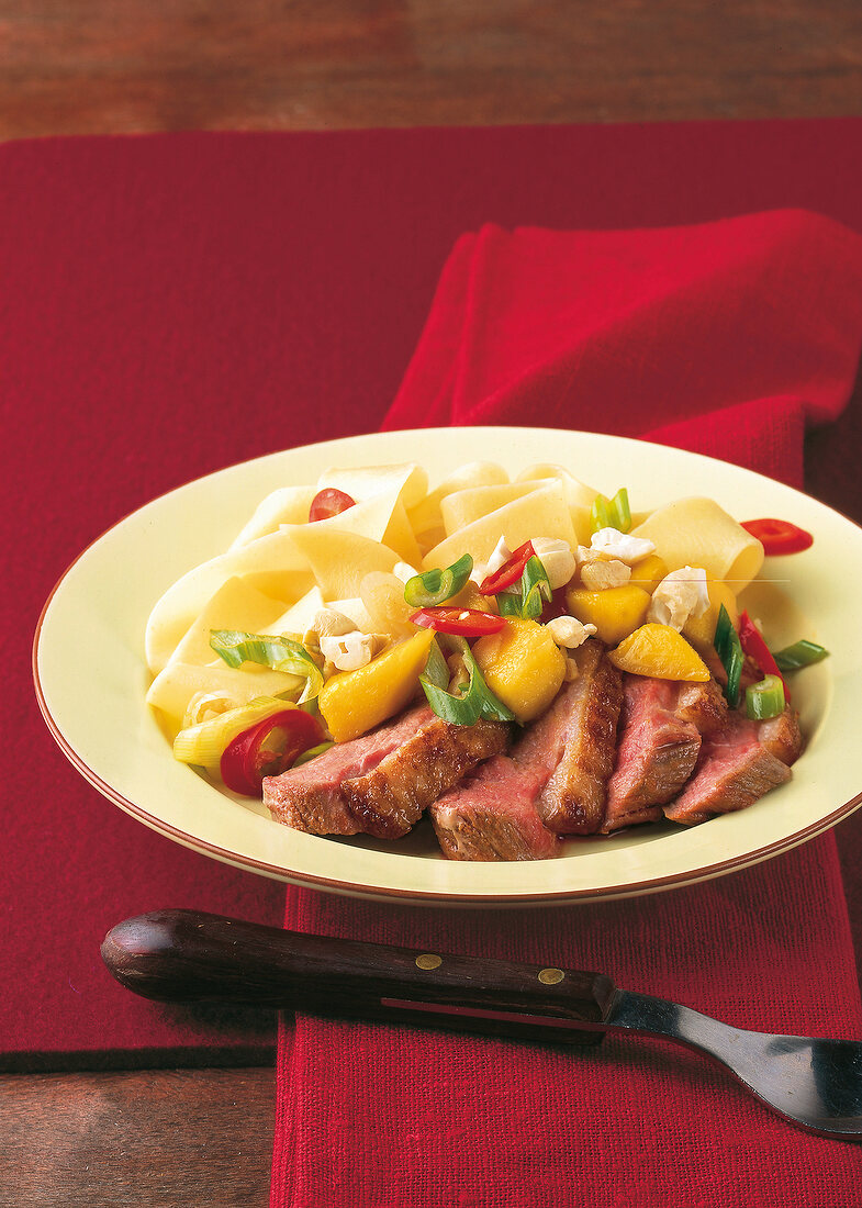 Duck breast with noodles, mango and cashew nuts on plate