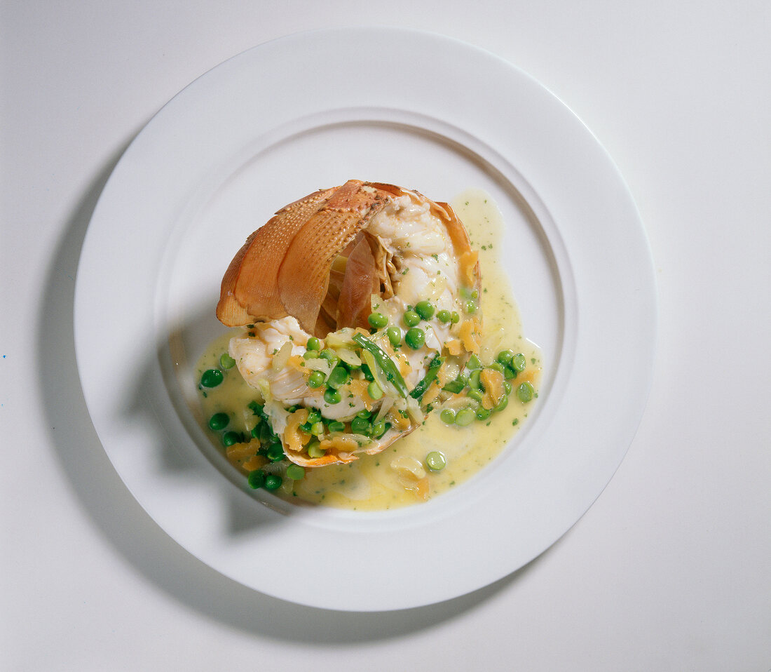 Steamed lobster with vegetables in butter sauce and peas on plate