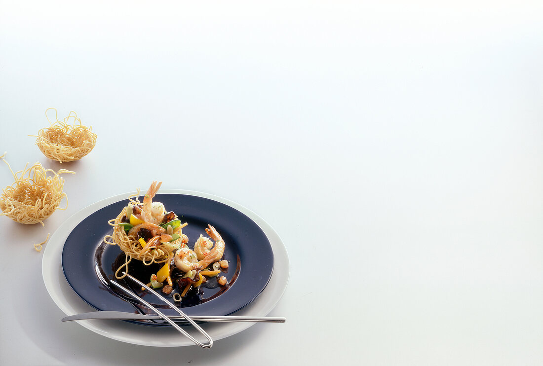 Ragout of shrimp and vegetables on plate with noodle basket, copy space