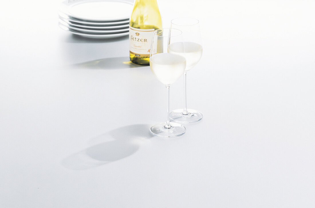 Plates, bottle and glasses of white wine on white background