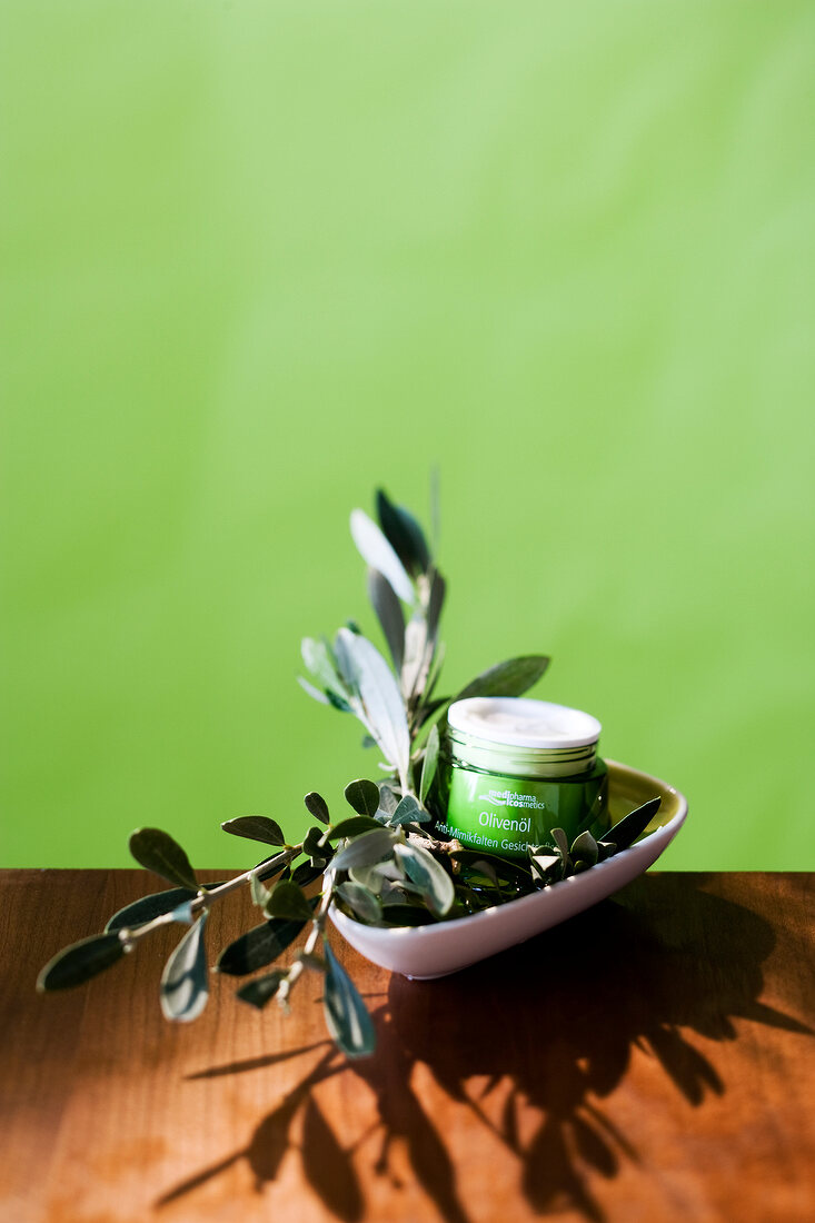 Close-up of bowl with olive oil cream and olive branch kept on wooden table