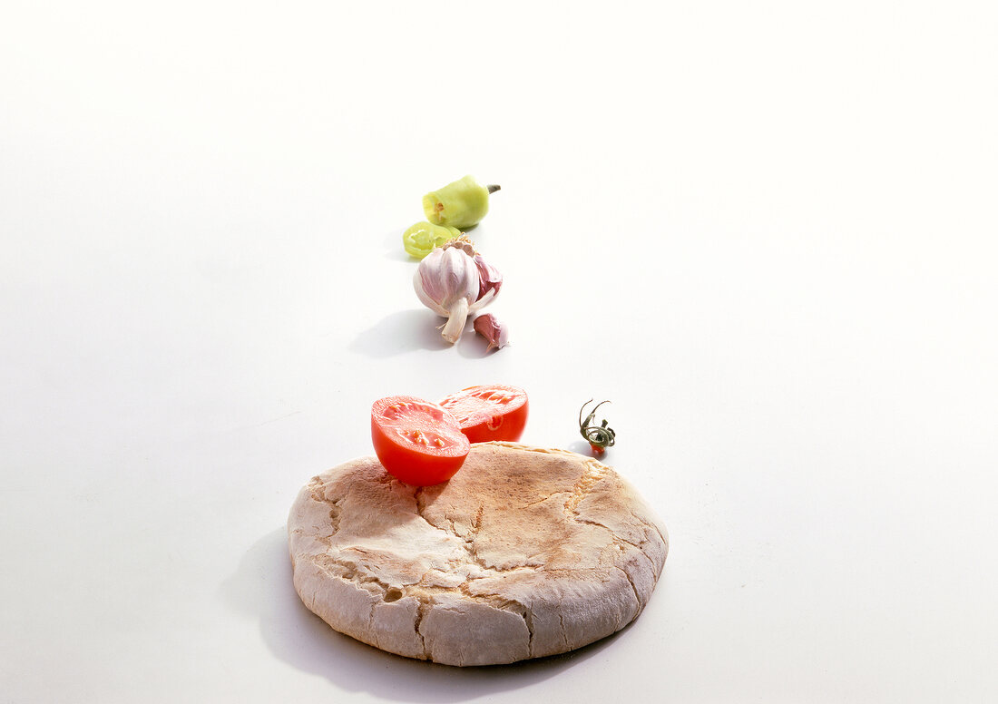 Round sour bread dough with tomato, garlic and hot peppers on white background