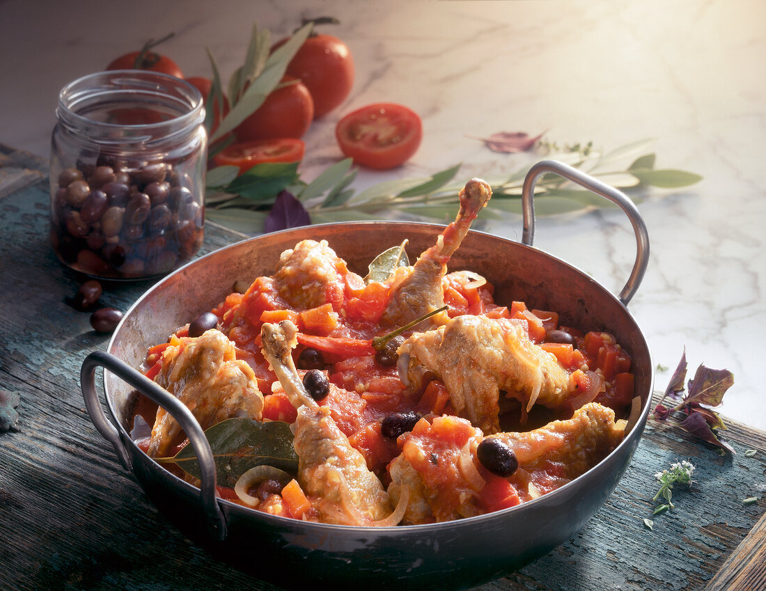 Guinea fowl in wine with tomatoes and olives in pan