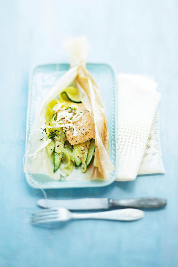 Baked salmon wrapped in parchment paper on tray