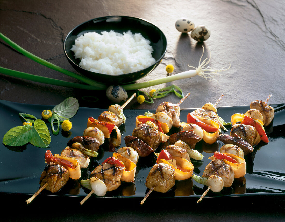 Grilled chicken on skewers and rice in bowl with quail eggs