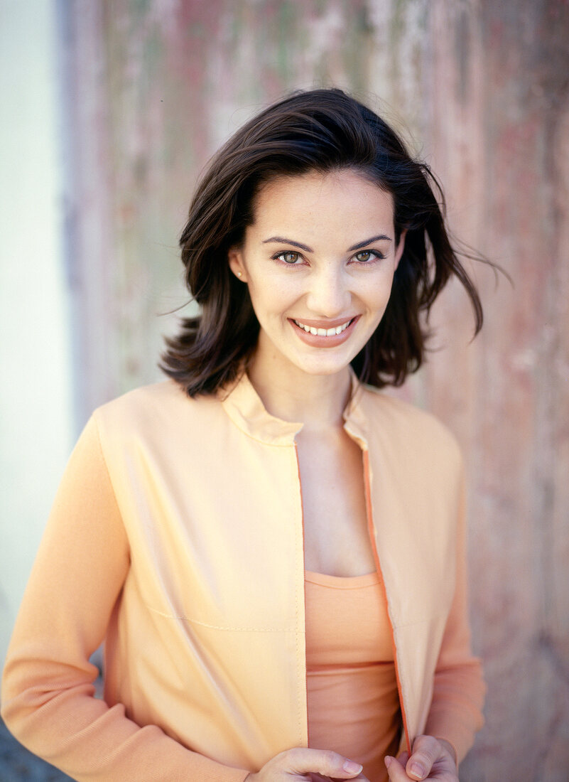 Portrait of pretty woman with dark hair standing in front of wooden wall, smiling