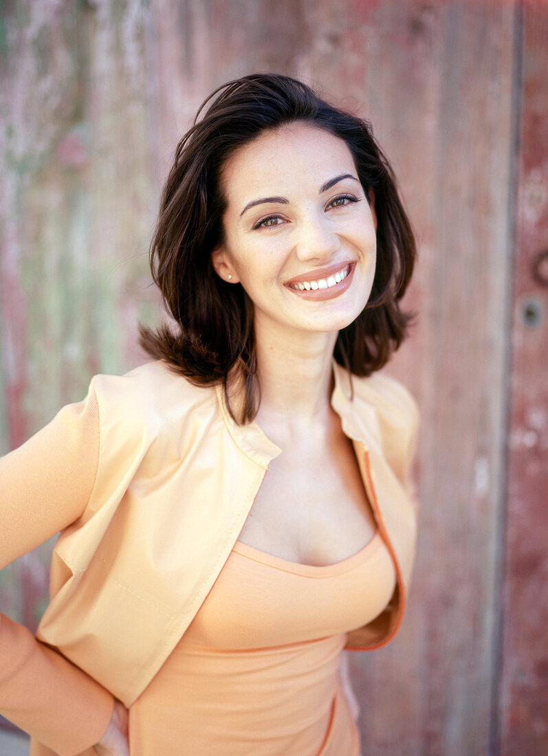 Portrait of pretty woman with dark mid length hair standing with hands on hips, smiling