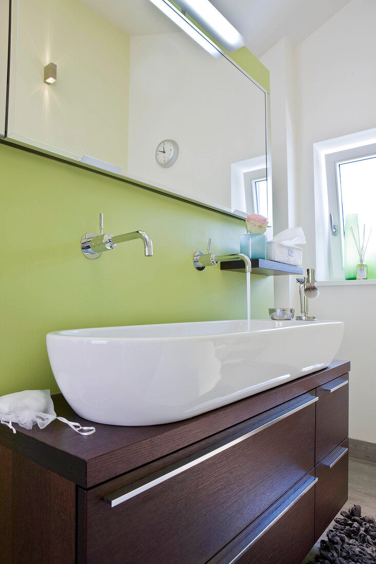Weißes, langes Waschbecken, brauner Waschtisch, grüne Wand, Spiegel