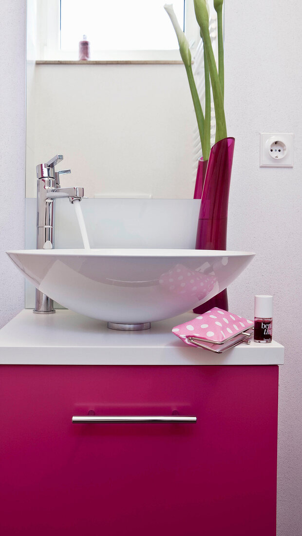 White washbasin, pink basin cabinet, mirror and pink flower vase