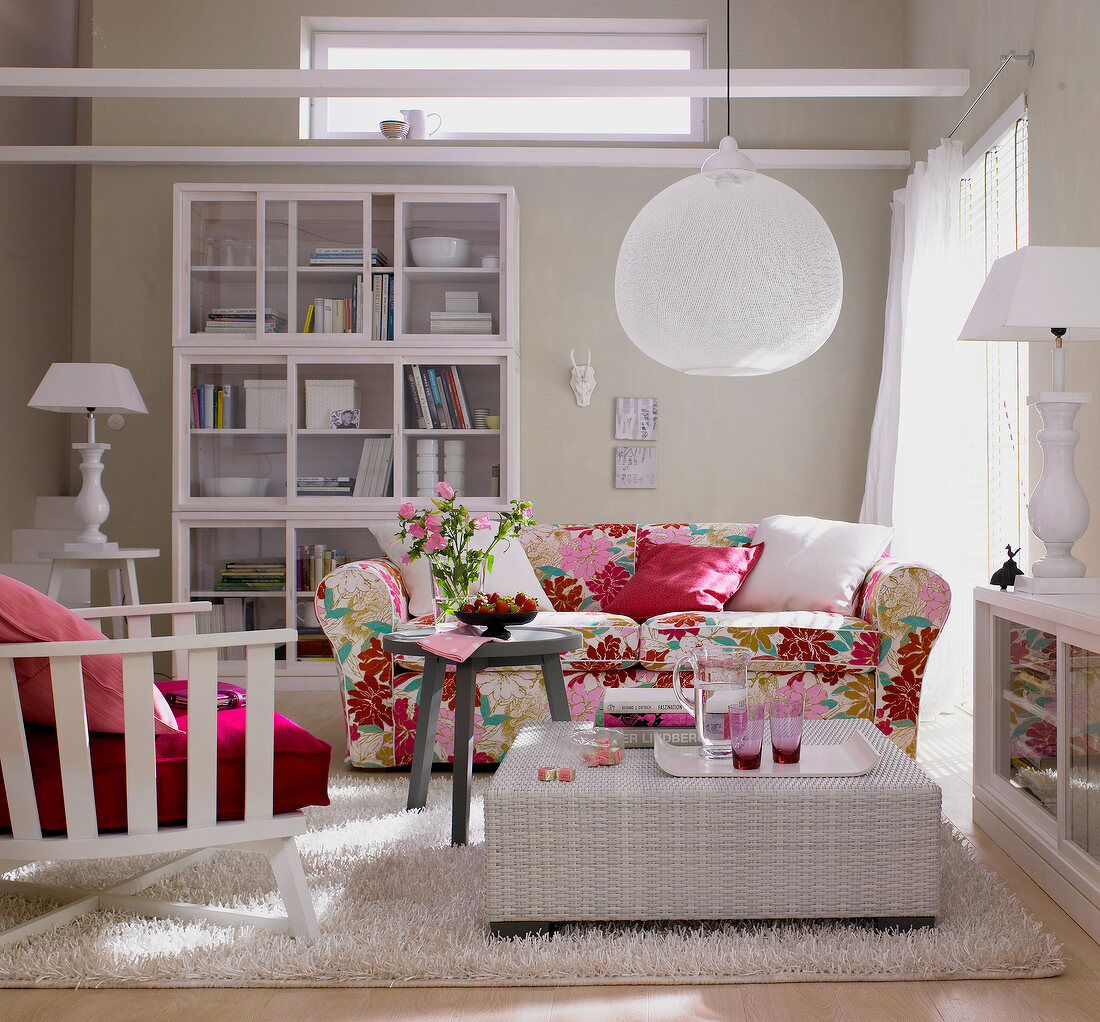 Living room in white with floral pattern couch, wicker table, china cabinet and lamp