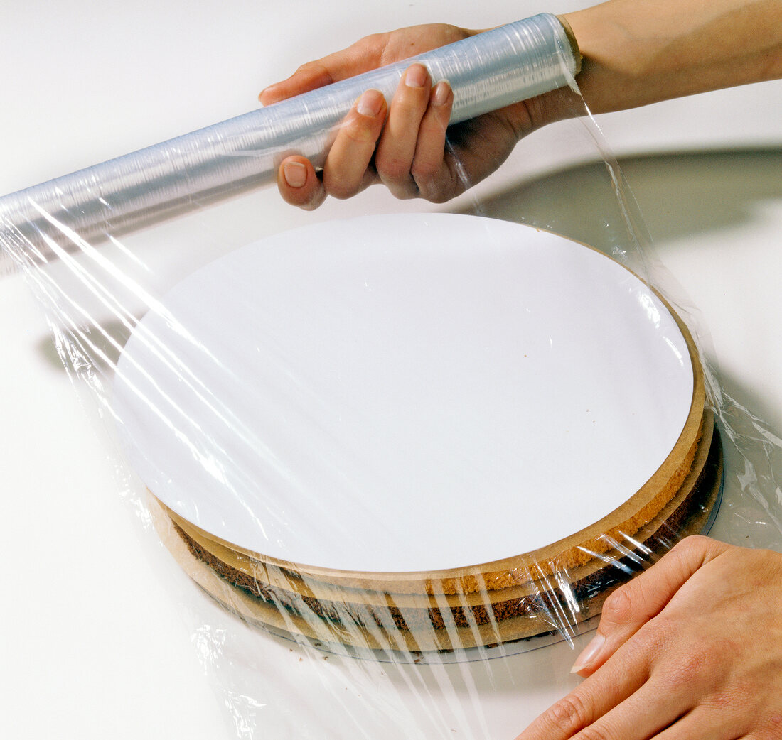 Close-up of hand wrapping layers of sponge cake with cellophane, step 4