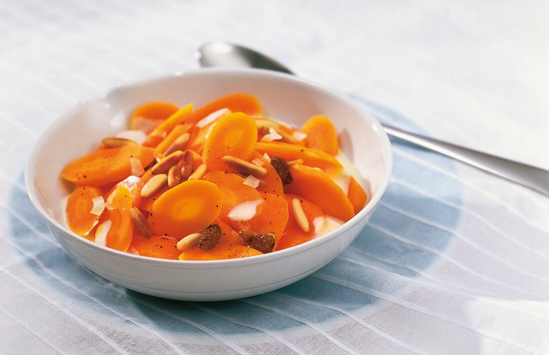 Bowl of sliced carrots with pine nuts and raisins in cream cheese