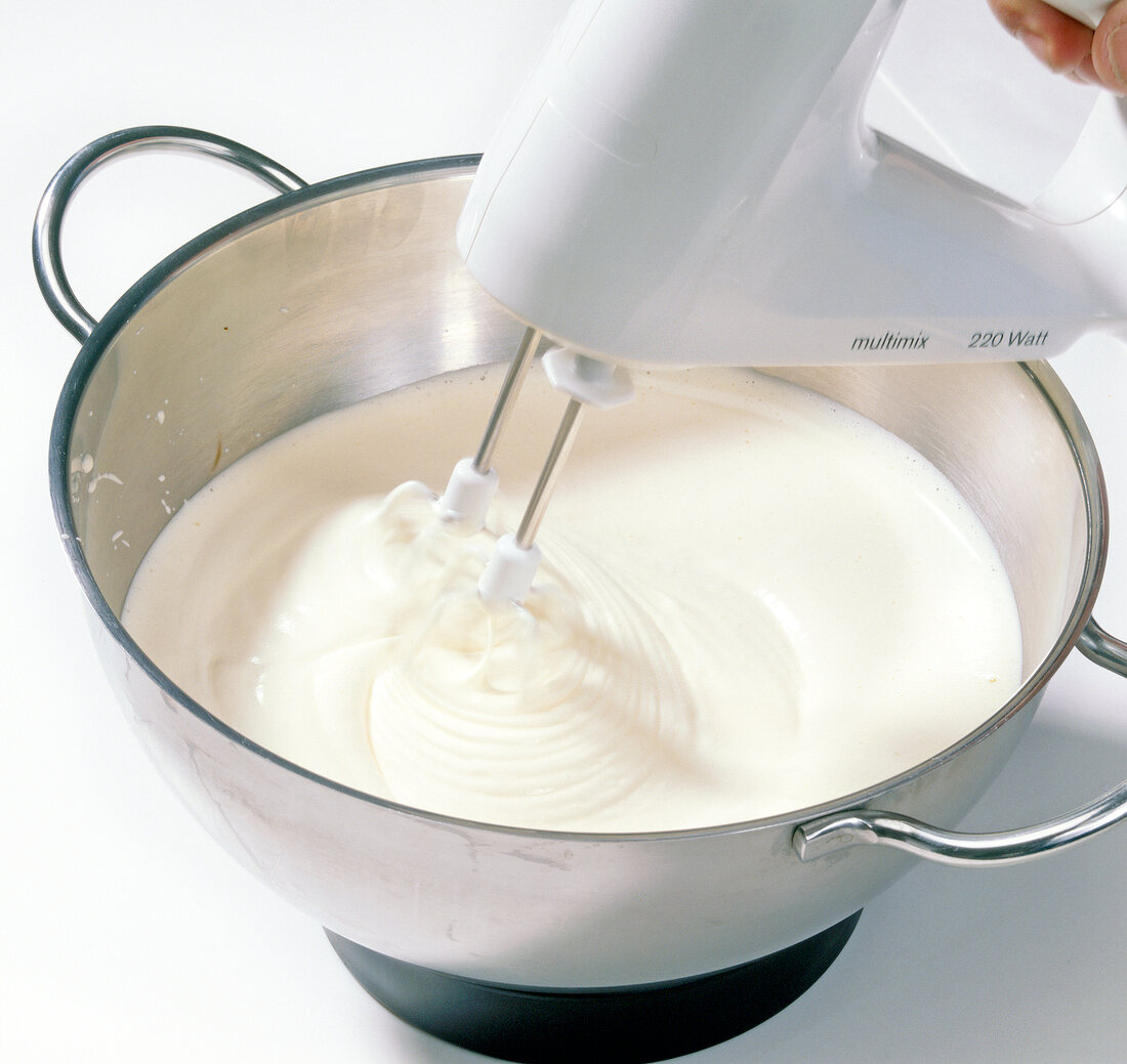 Close-up of cream being beaten in pan with beater for preparation of chocolate, step 2